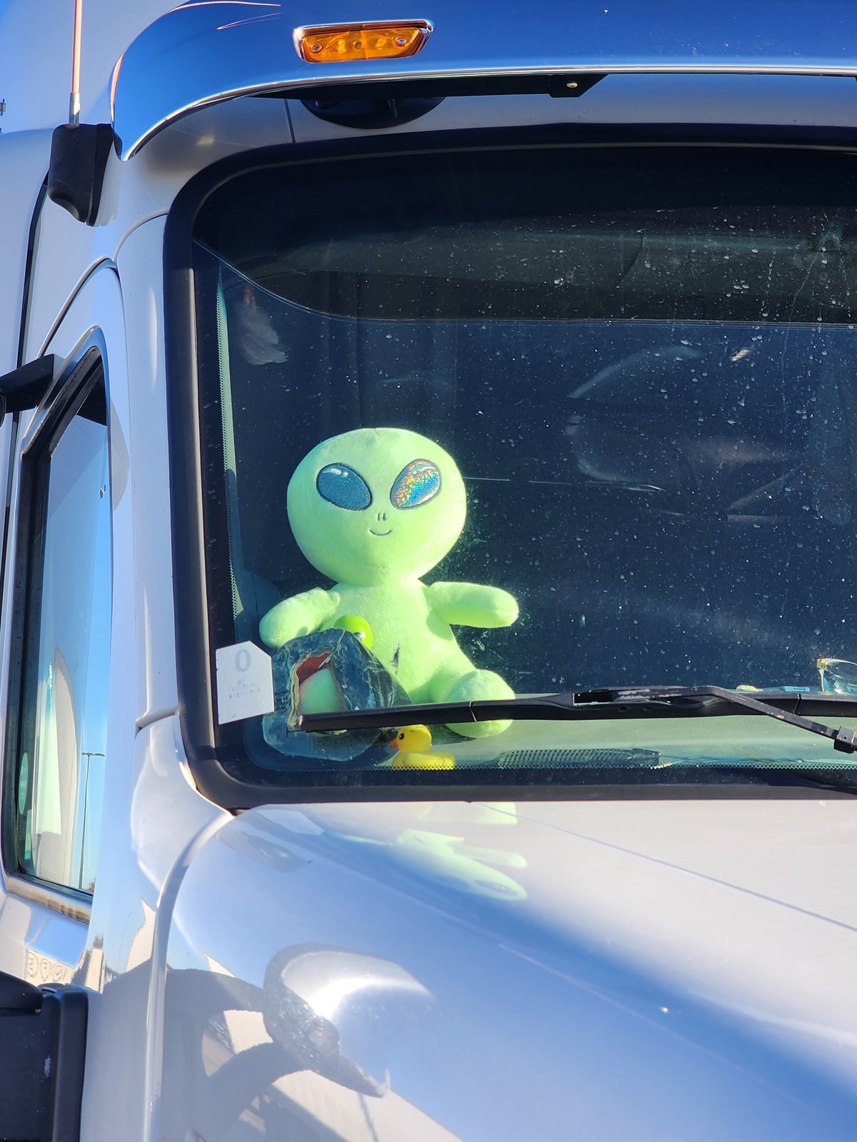 A green alien plush toy stuck to the inside of the windscreen of the truck of Bill, looking out at the road