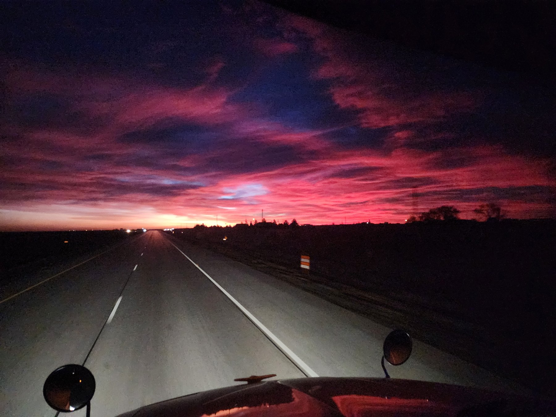 The view from inside the cab of Wild Bill at dawn, an open highway running toward a burning red and purple horizon