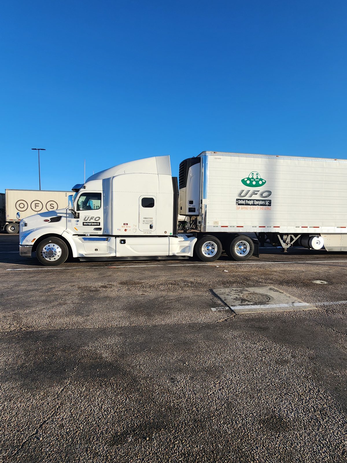 the white UFO tractor of Bill and reefer parked on gravel at a truck stop under a clear sky