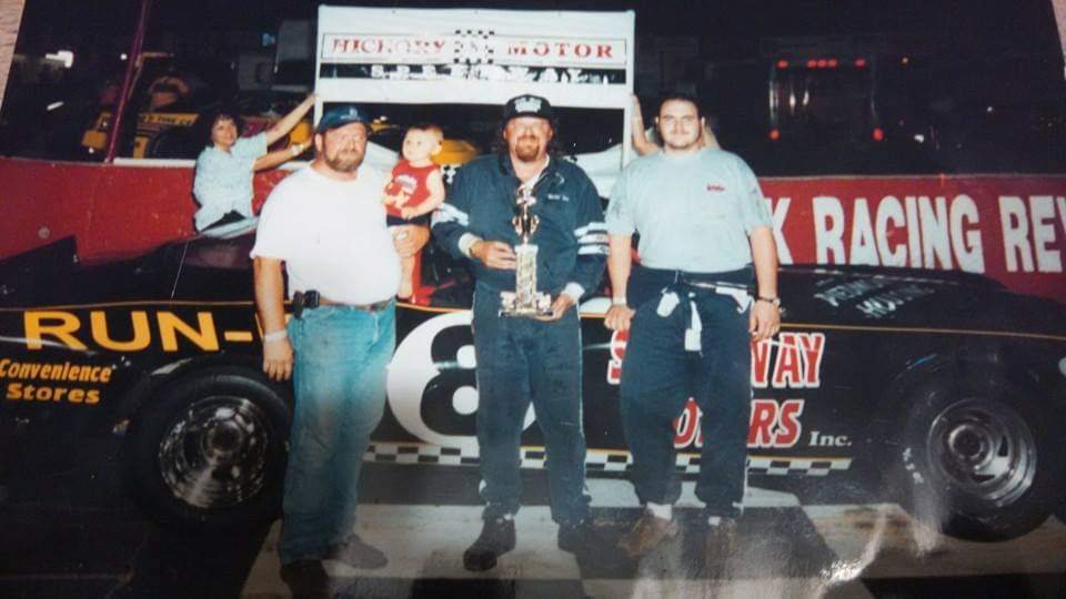 Bill in victory lane at Hickory Motor Speedway, holding a trophy beside his number 8 late model stock car, with family behind him